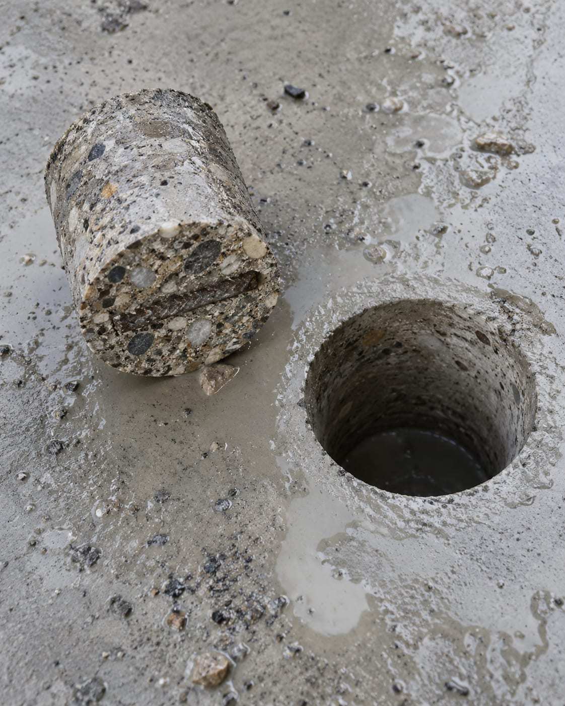 Frisch gebohrter Betonkern liegt neben dem runden Bohrloch in einer Betonplatte